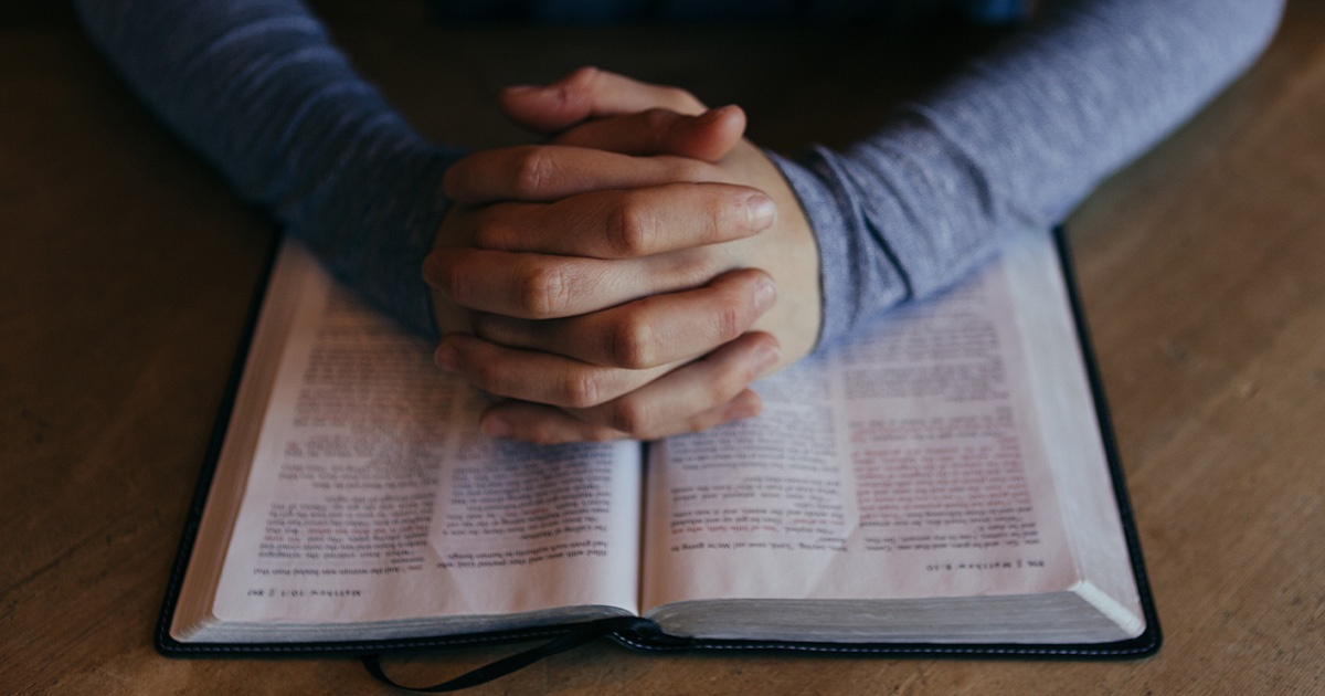 Hands praying over a Bible