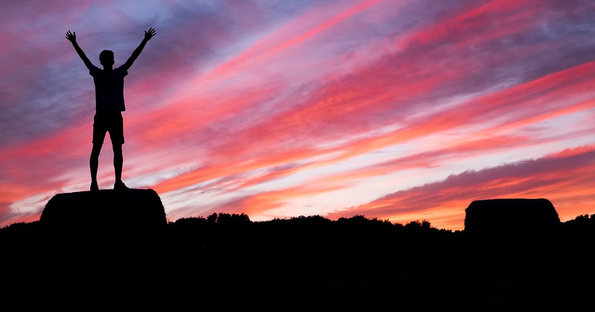 A man raising his arms on a mountain top, representing determination and perseverance