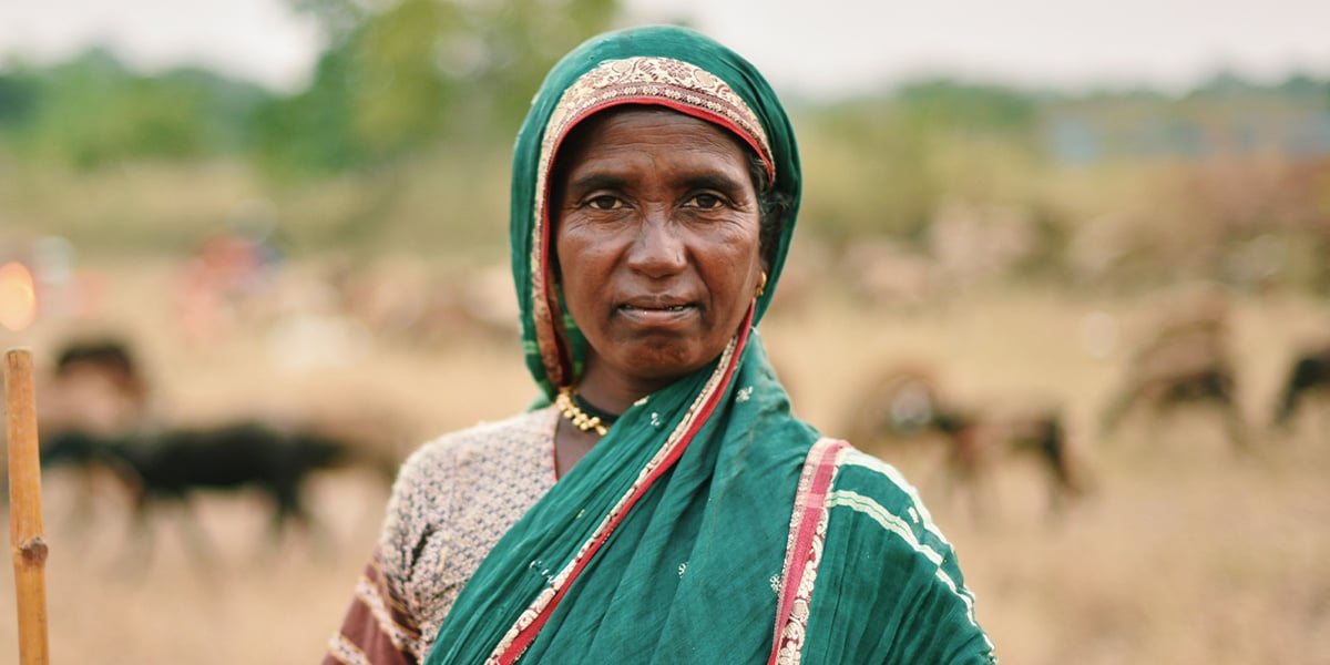 Southeastern Asain woman standing in front of a farm wearing a green cloth wrapped around her head and shoulder.